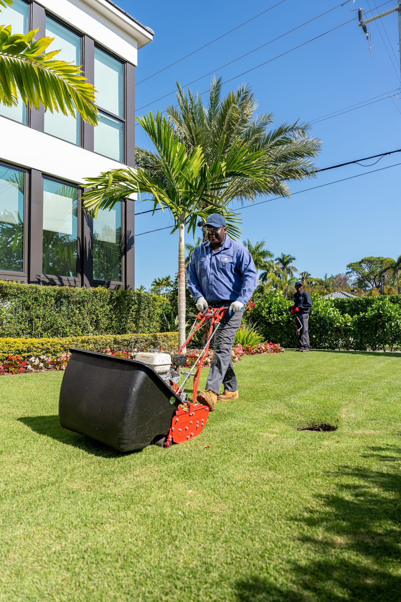 Coastal Cares technician mowing a manicured lawn beside a pool deck